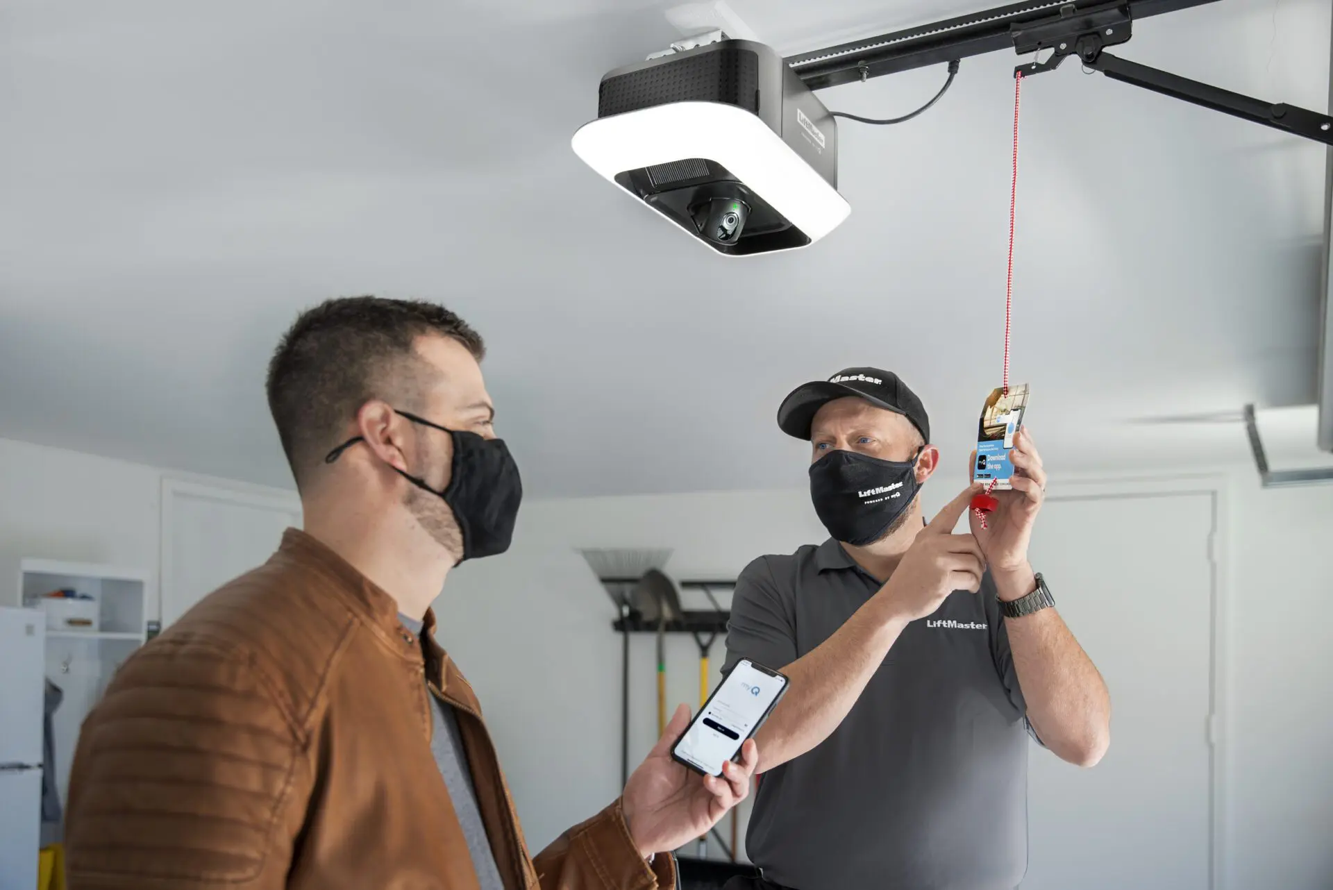 Two men wearing masks are looking at a phone.