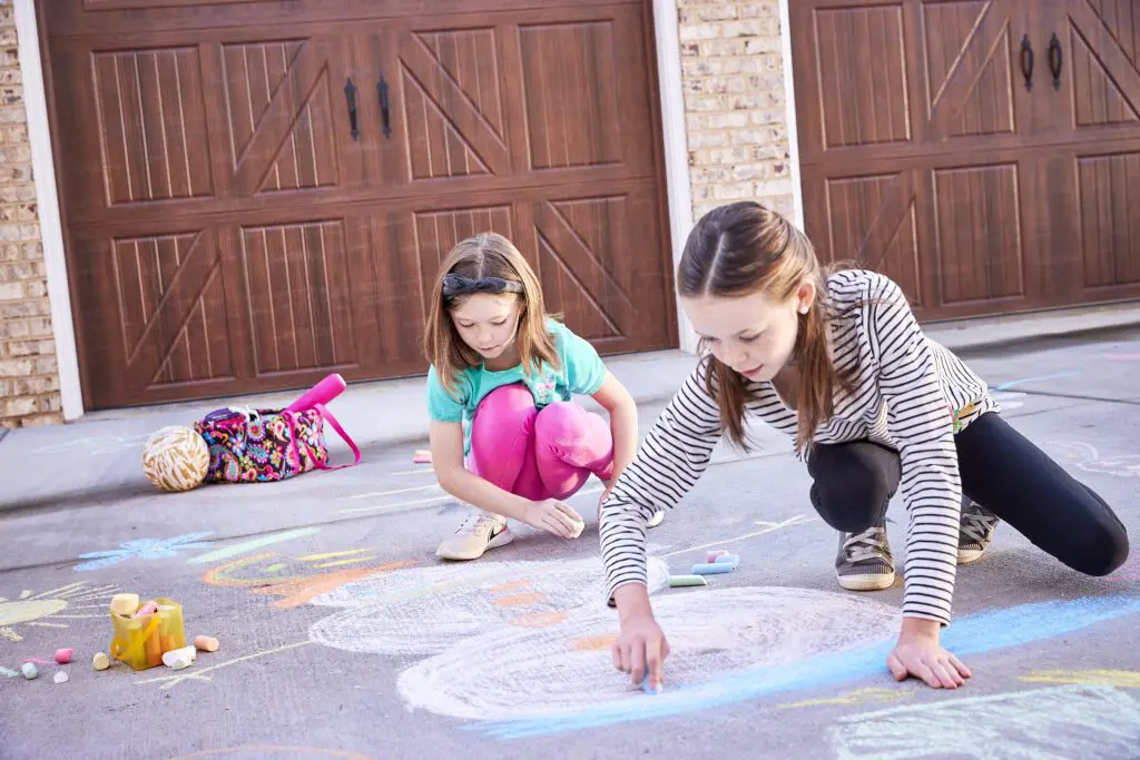 Two girls drawing with chalk on the ground.