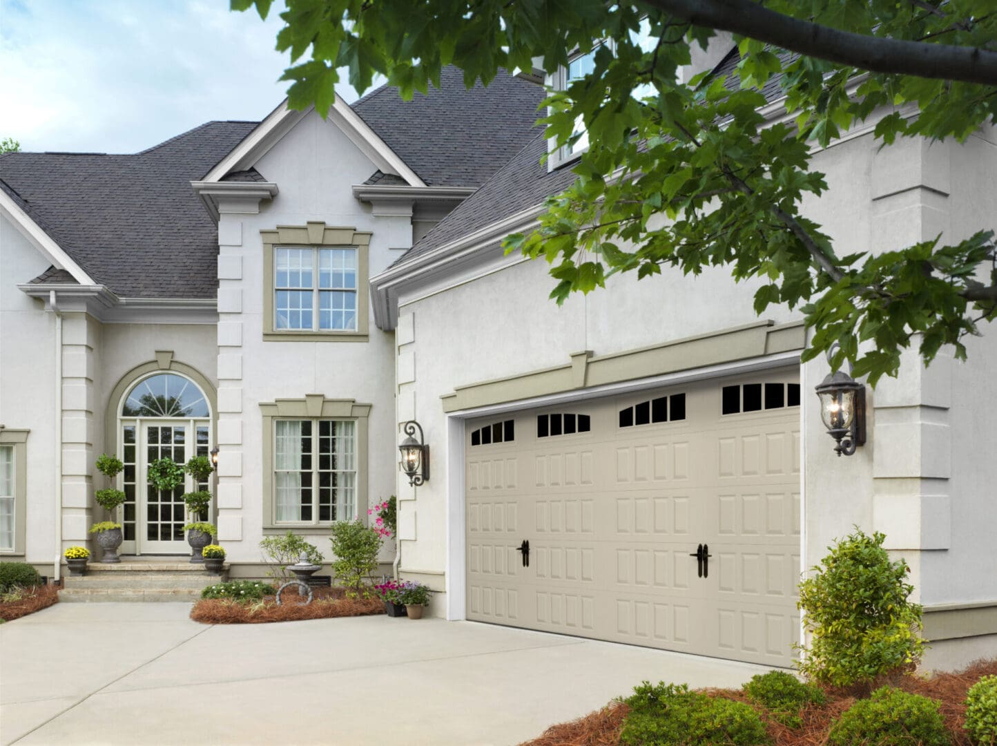 Modern white two-story house with a prominently featured, closed beige garage door, complemented by a well-maintained driveway and green landscaping.